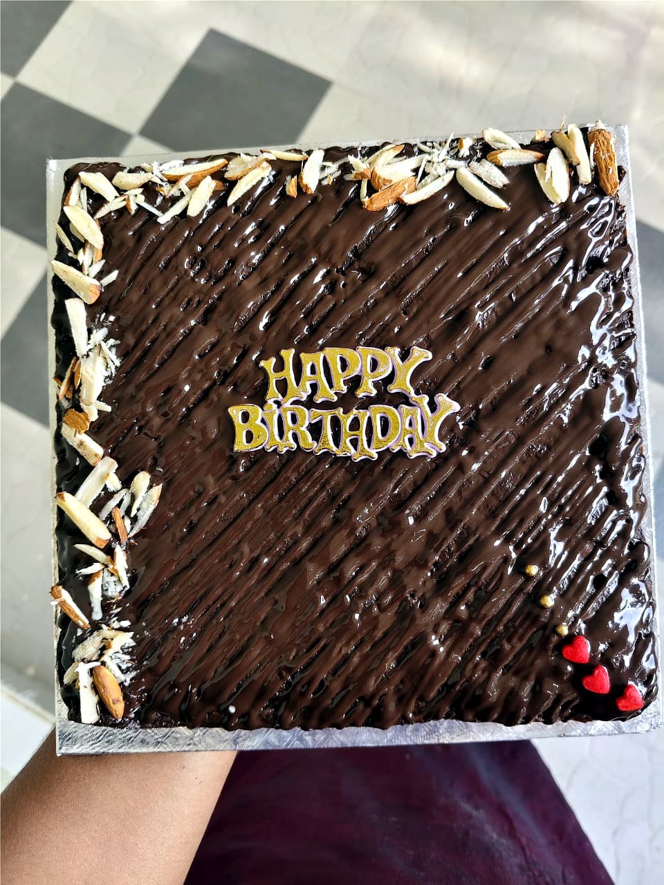 Square chocolate birthday cake with glossy ganache, almond flakes and a gold Happy Birthday topper