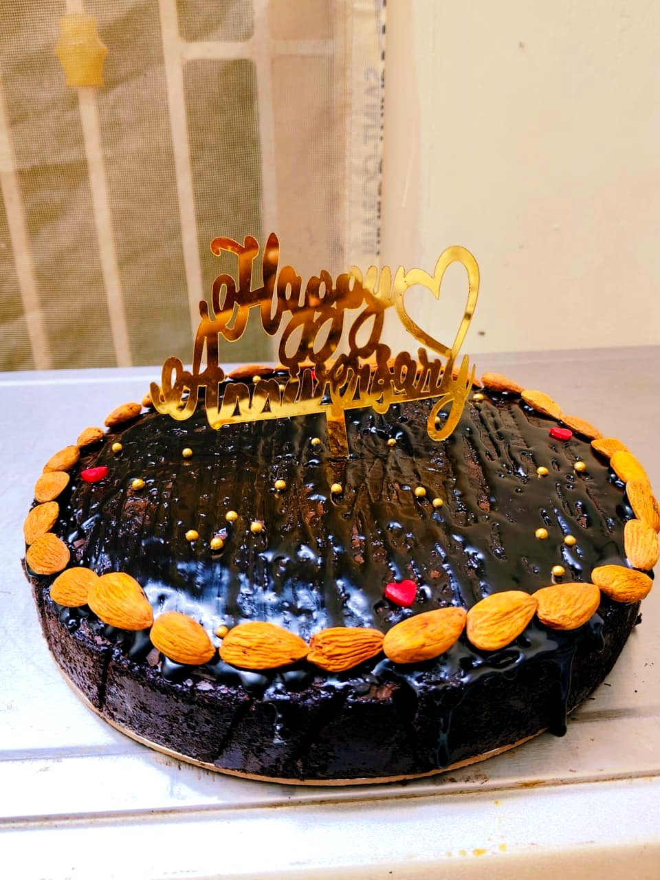 Round chocolate anniversary cake ringed with almonds, gold pearls and a golden Happy Anniversary topper